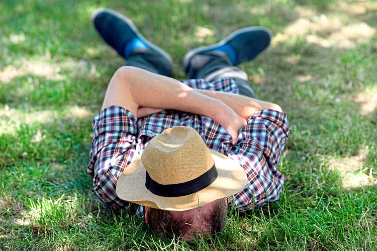 Ein Schläfer schläft im Gras, ein Hut deckt sein Gesicht ab