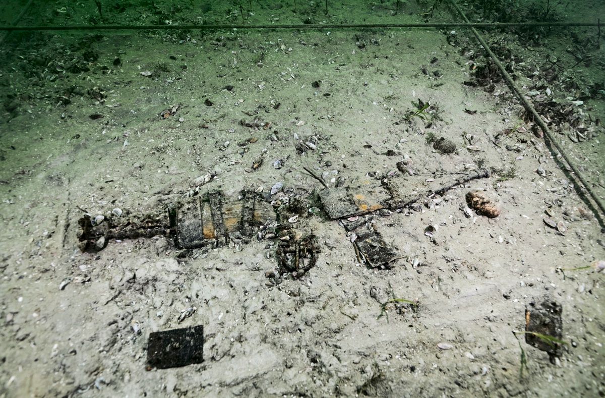 Unterwasseraufnahme von römischen Fundstücken am Grund des Neuenburgersees in Neuchâtel, umgeben von Sand, Muscheln und Pflanzenresten.