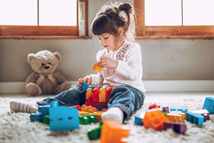 Kleines Mädchen sitzt auf dem Teppichboden und spielt mit Bausteinen