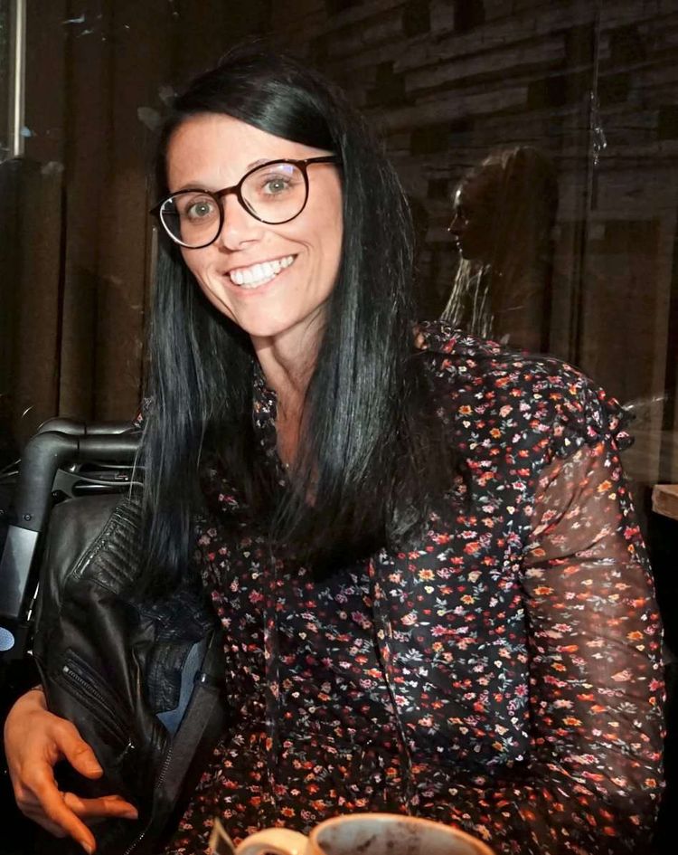 Junge Frau mit schwarzen Haaren und Brille lächelt in die Kamera