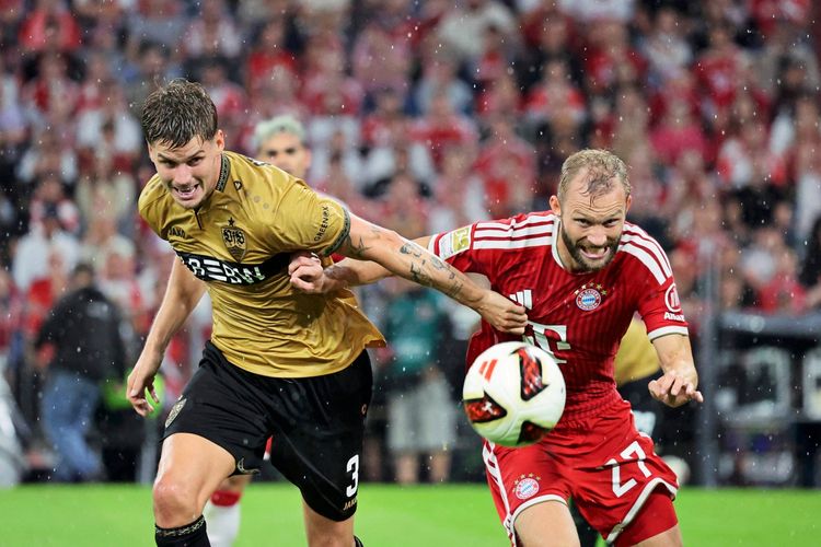 Zwei Fußballspieler kämpfen während eines Bundesligaspiels zwischen dem FC Bayern München und dem VfB Stuttgart am 28. August 2026 in München um den Ball. Der Spieler in rotem Trikot (Bayern München) und der Spieler in goldenem Trikot (VfB Stuttgart) befinden sich im regenreichen Stadion.