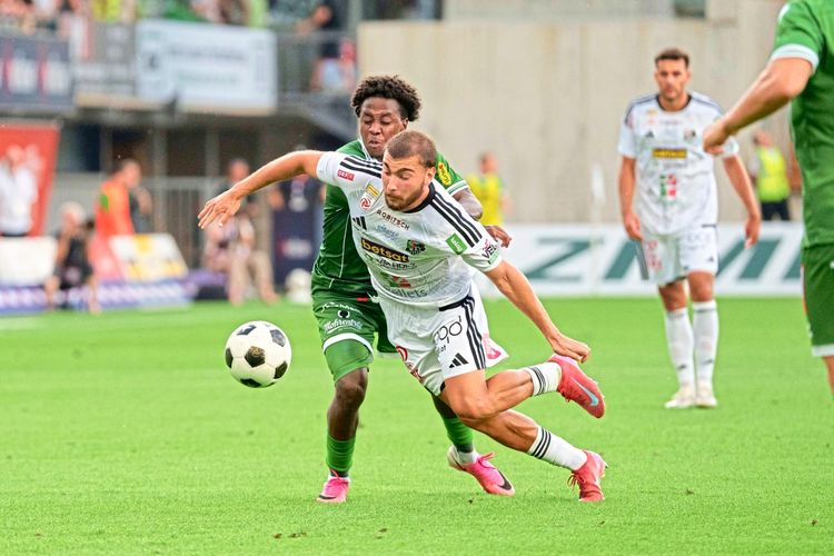 Zwei Fußballspieler kämpfen um den Ball während eines Spiels der österreichischen Bundesliga zwischen SC Austria Lustenau und RZ Pellets WAC am 15. August 2026. Ein Spieler in grün (Lustenau) und ein Spieler in weiß (WAC) sind in einer intensiven Aktion auf dem Spielfeld. Im Hintergrund sind weitere Spieler und Zuschauer zu sehen.