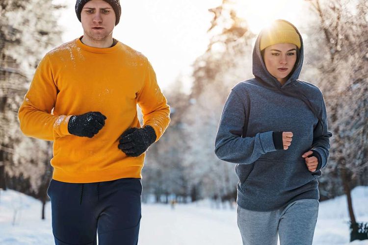 Ein junger Mann und eine junge Frau joggen in Trainingsanzügen durch den Schnee