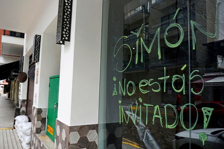 Ein Geschäft in Puerto Vallarta, Jalisco, Mexiko, mit einem handgeschriebenen Schild auf der Glasscheibe, das mit grüner Schrift „Simón, no estás invitado“ (Simón, du bist nicht eingeladen) sagt. Dieses bezieht sich auf den Hurrikan Simón, der laut dem nationalen Wetterdienst Mexiko bedroht. Sandtaschen sind am Boden zu sehen.