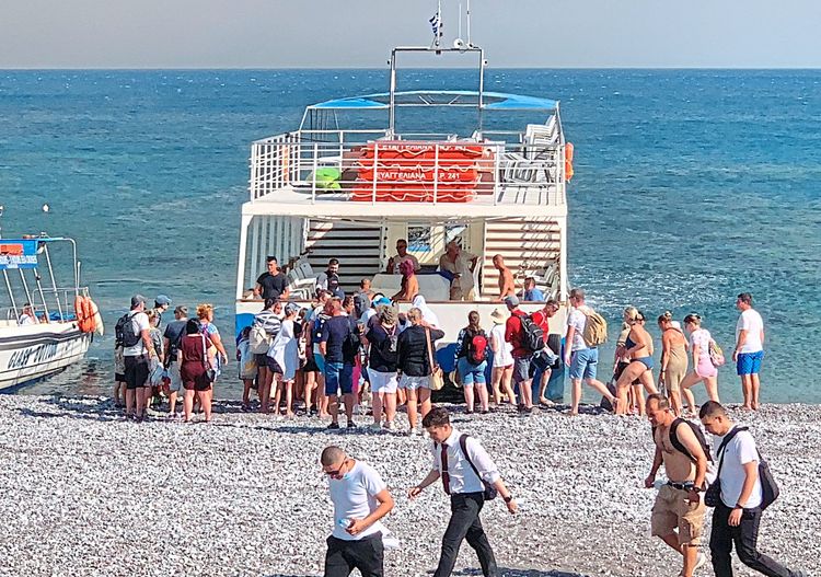 Ein Schiff ist am Strand zu sehen. Davor stehen Touristen, die auf ihre Evakuierung warten.