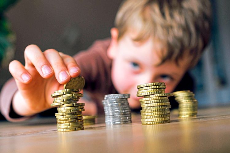 Ein fünfjähriger Junge stapelt Kleingeld auf einem Tisch.
