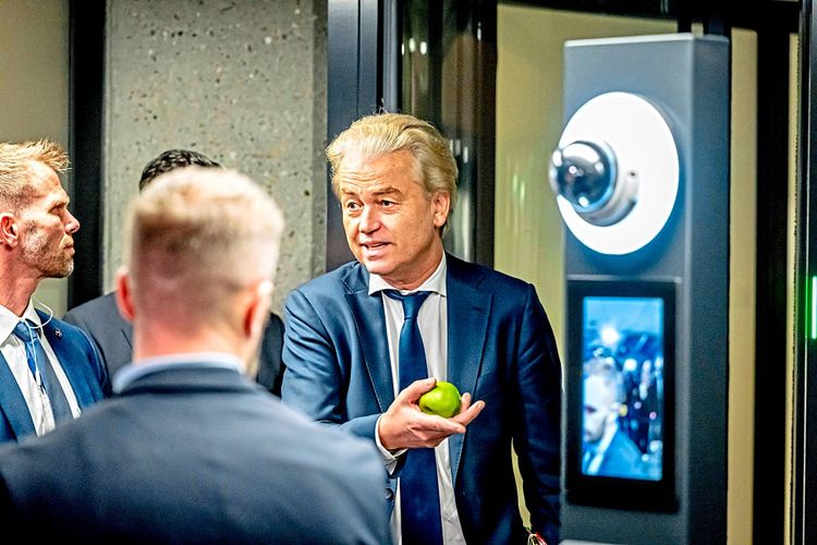 Geert Wilders vor Mikrofonen, hält etwas grünes, rundliches in seinen Händen