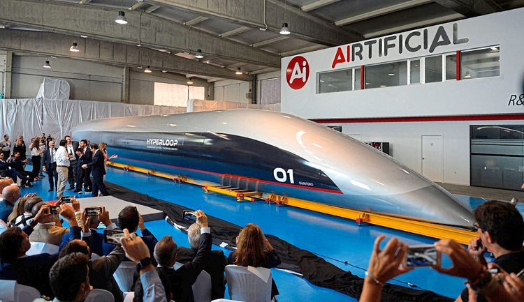 Hyperloop-Zug steht auf einer Tribüne in einer Halle, Zusehende fotografieren den Zug.