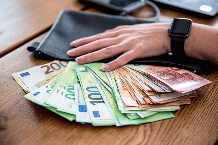 Diverse Euro-Geldscheine liegen auf einem Tisch aufgefächert, eine Männerhand liegt darauf