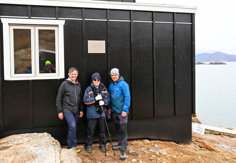 Drei Männer stehen vor der schwarzen Außenwand der neuen österreichischen Forschungsstation in Grönland