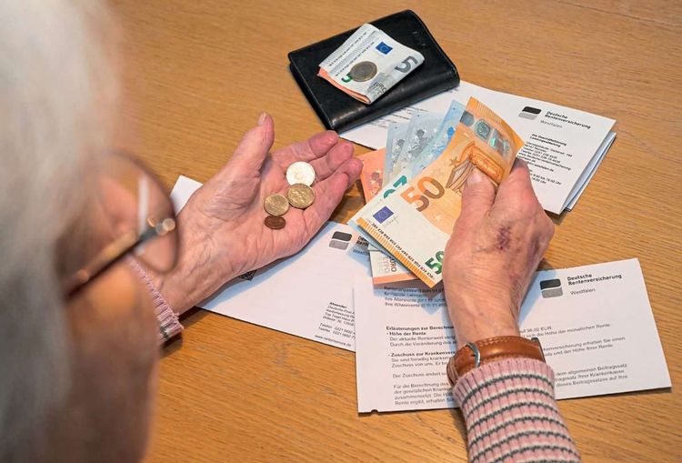 Ältere Frau hat Münzen und Geldscheine in der Hand.