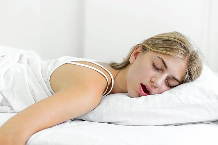 Blonde Frau schläft auf weißer Bettwäsche mit geöffnetem Mund 