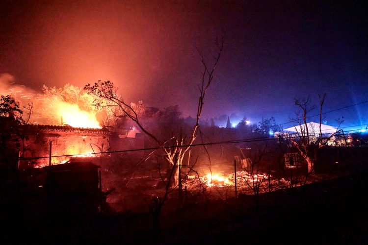 Brennendes Haus bei Nacht in Cotignac, Südfrankreich, umgeben von Flammen und Rauch. Im Hintergrund sind beleuchtete Gebäude und dunkle Silhouetten von Bäumen sichtbar.
