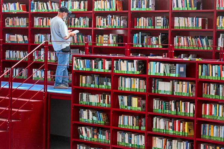 Ein Mann betrachtet ein Buch in der renovierten Bibliothek des Corviale in Rom, Italien. Die Bibliothek wurde in ein bioklimatisches Schutzgebäude umgewandelt, als Teil eines EU-geförderten Projekts zur Verbesserung der Klimawiderstandsfähigkeit und sozialen Integration für etwa 4.500 Bewohner. Die Regale sind rot und mit Büchern gefüllt. Datum: 15. Juli 2026.