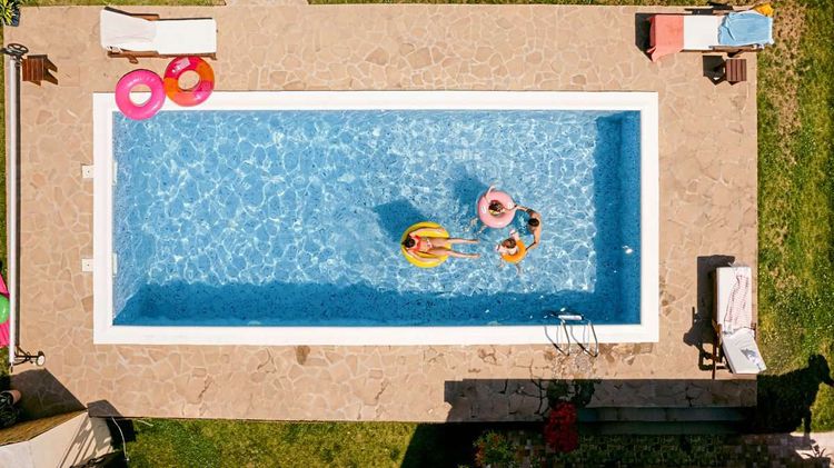 Ein Pool aus der Vogelperspektive in dem eine Familie auf bunten Schwimmreifen schwimmt.