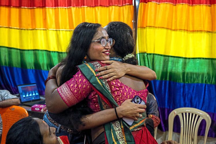 Zwei Frauen im Sari umarmen sich vor einer Regenbogenflagge