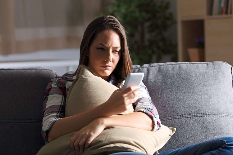 Frau sitzt auf Couch und schaut verängstigt auf ein Handy