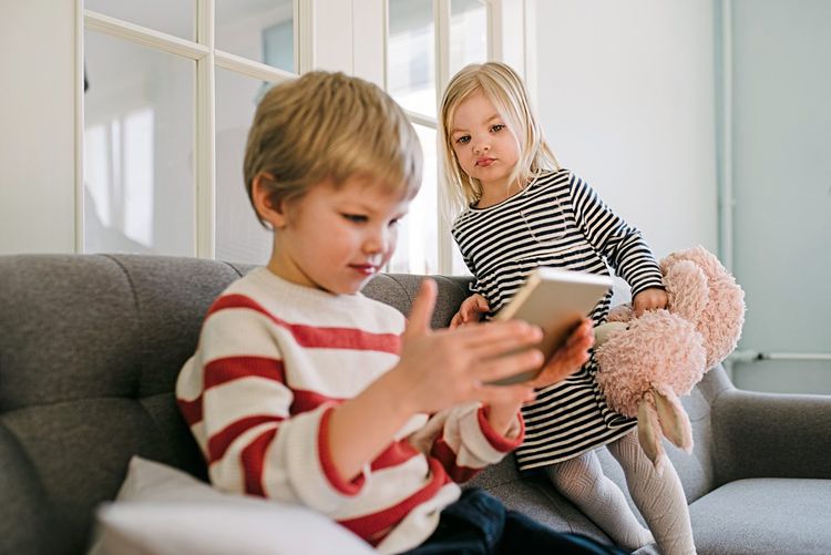 Ein Bub und ein Mädchen (beide etwa 3 oder 4 Jahre) sitzen auf dem Sofa und schauen auf ein Tablet