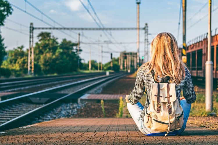 Junge Frau mit Rucksack sitzt auf dem Bahnsteig und wartet auf Zug