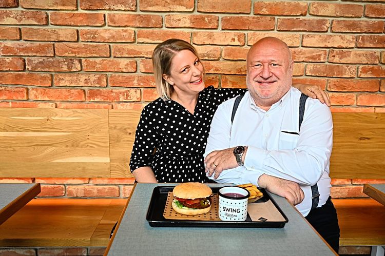 Das Ehepaar Charly und Irene Schillinger in einem ihrer nostalgisch eingerichteten Fastfoodrestaurant in Wien Vor ihnen steht ein veganer Burger auf einem Tablett.