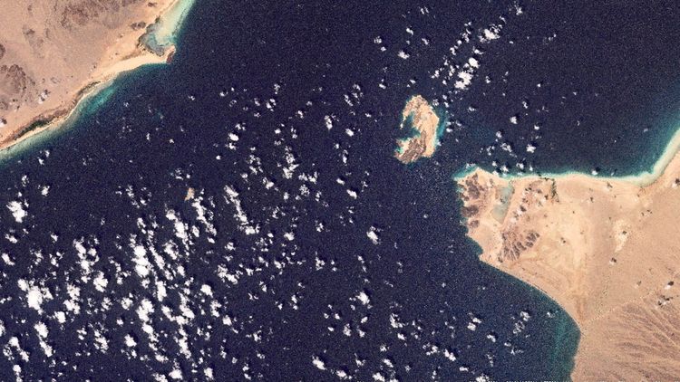 Satellitenbild der Meerenge Bab al-Mandab vor der Küste des Jemen, mit einer kleinen Insel in der Mitte und Wüstenlandschaft an den Ufern. Dünne Wolken sind über das dunkelblaue Wasser verteilt.