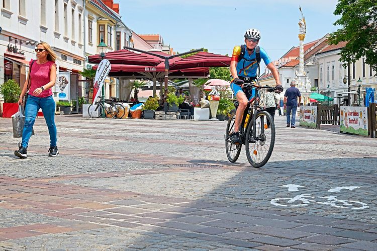 Eine Fußgängerin und ein Radfahrer am Hauptplatz von Eisenstadt.
