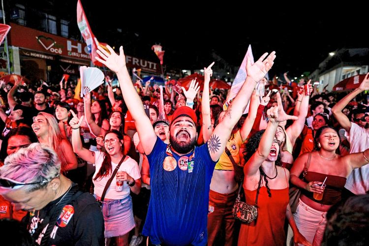 Menschenmenge aus begeisterten Unterstützern mit Fahnen und Schildern, jubelnd und feiernd bei einer Wahlveranstaltung in Brasilien bei Nacht.
