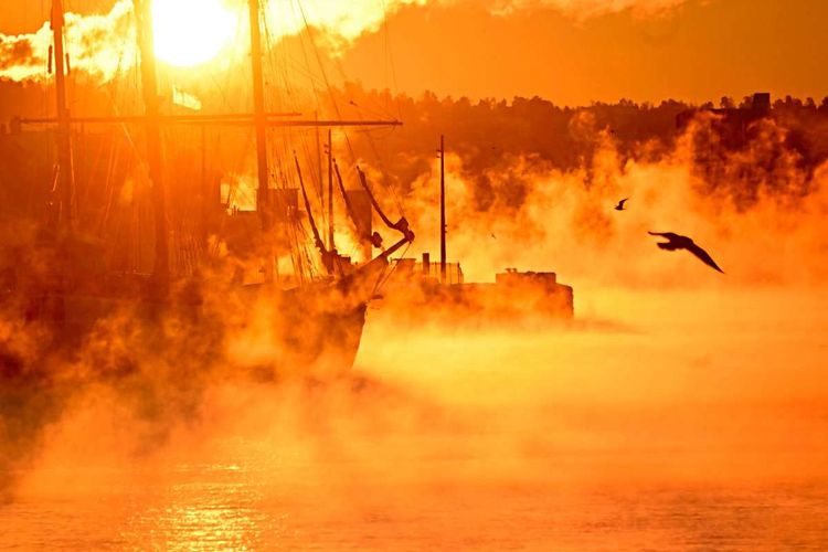 Wasserdampf steigt im orangefarbenen Morgenlicht auf zwischen historischen Schiffen