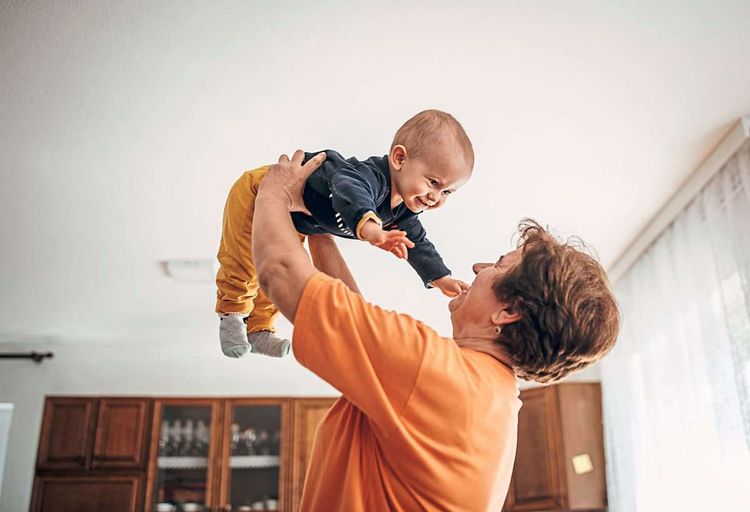 Eine Oma hält ihr kleines Enkelkind in die Luft und lacht