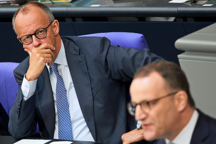 Zwei Männer in einem Sitzungsraum im Bundestag. Der Mann im Hintergrund blickt nachdenklich nach vorne und stützt sein Gesicht mit der Hand. Der Mann im Vordergrund spricht und ist unscharf abgebildet.
