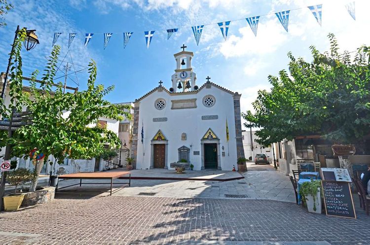 Kleine weiße Kirche am Dorfplatz mit Griechenland-Wimpeln im Vordergrund