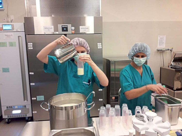 Zwei Frauen in Klinikkleidung udn Mundschutz gießen Muttermilch in Flaschen