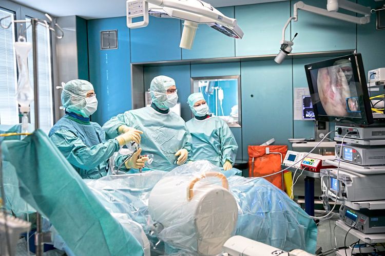 Ein Operationssaal mit drei Personen, die eine Sonde in den Körper des Patienten eingeführt haben und auf einen Bildschirm blicken