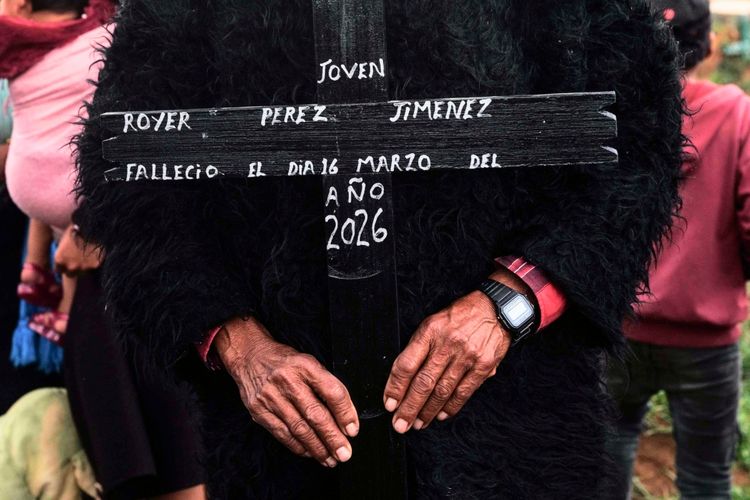 Ein Mann hält während einer Beerdigung im Tzotzil-indigenen Dorf San Juan Chamula, Chiapas, Mexiko, ein Holzkreuz mit der Aufschrift „Royer Pérez Jiménez“ in den Händen. Das Kreuz erinnert an einen 19-jährigen Mexikaner, der am 16. März 2026 in einem US-Haftzentrum gestorben ist. Im Hintergrund sind Trauernde zu sehen.