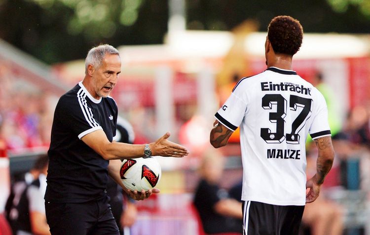 Eintracht Frankfurt-Trainer in schwarzem Trainingsoutfit spricht mit einem Spieler im weißen Trikot mit der Aufschrift 