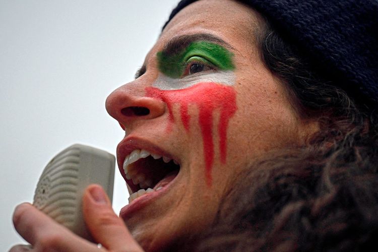 Frau mit ins Gesicht geschminkter iranischer Flagge in Tränenform