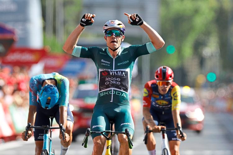 Belgischer Radfahrer in grünem Trikot jubelt mit erhobenen Armen als Sieger der 15. Etappe der Vuelta a España 2026, gefolgt von zwei weiteren Fahrern im Ziel.