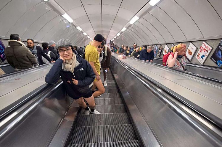 Menschen fahren mit einer Rolltreppe an einem Bahnhof nach oben. 