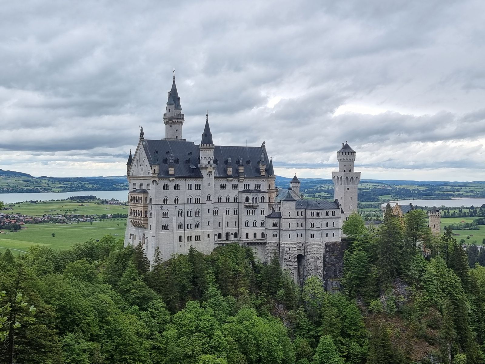 Ein historisches Gebäude auf einem Felsstock mitten in der grünen Landschaft, darüber ein wolkenverhangener Himmel