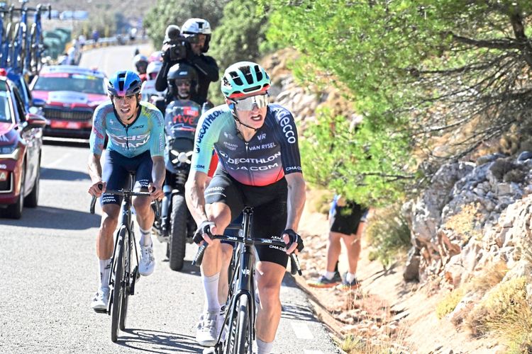 Zwei Radrennfahrer in Wettkampfbekleidung fahren während der 9. Etappe der Vuelta a España 2026 auf einer bergigen Straße. Im Hintergrund sind Teamfahrzeuge, ein Motorrad mit Kameramann und Zuschauer zu sehen. Die Strecke ist von Bäumen und Felsen gesäumt.