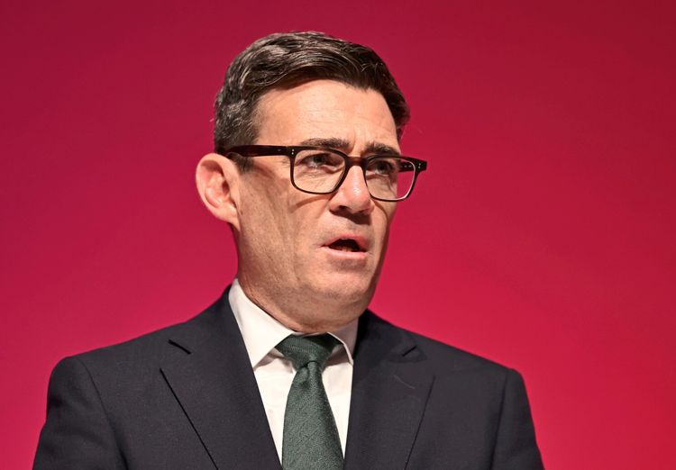 Eine Person mit Brille und Anzug spricht vor einem einfarbigen rosa Hintergrund.