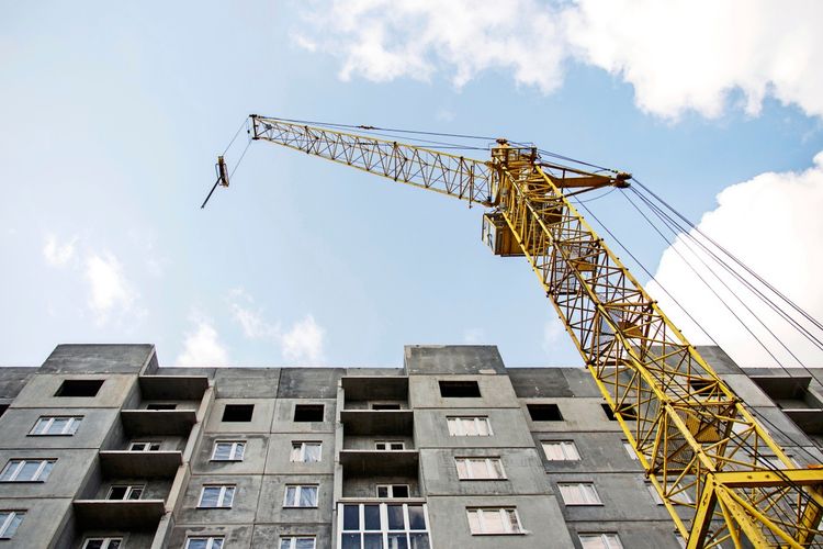 Eine große gelbe Turmkran steht neben einem im Bau befindlichen Beton-Wohngebäude, mit hellem Himmel im Hintergrund.
