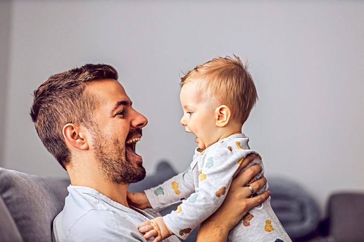 Vater spricht mit seinem Baby. Baby ahmt Mundbewegung des Vaters nach.