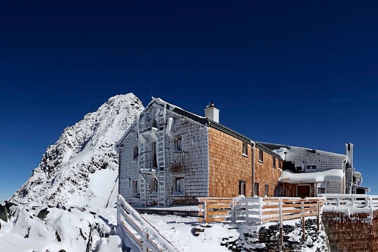 Die Erzherzog-Johann-Hütte auf der Adlersruhe (3454 m), umgeben von Schnee, mit Blick auf einen markanten Gipfel unter klarem blauem Himmel.