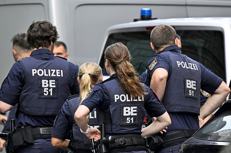 Eine Gruppe von Polizistinnen und Polizisten in Uniform, von hinten fotografiert, während eines Einsatzes in Wien. Auf ihren Westen sind das Wort 