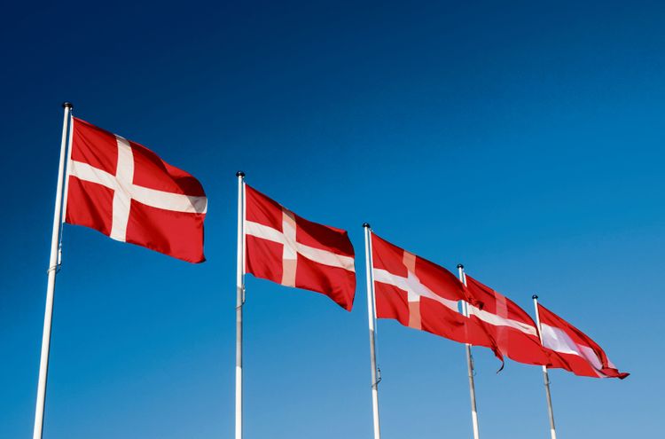 Dänische Flaggen auf Fahnenmasten, im Verlauf von links nach rechts gehen sie über in die österreichische.