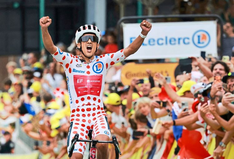 Radfahrer in gepunktetem Bergtrikot jubelt mit erhobenen Armen nach dem Gewinn der 20. Etappe der Tour de France. Im Hintergrund jubelnde Zuschauer.