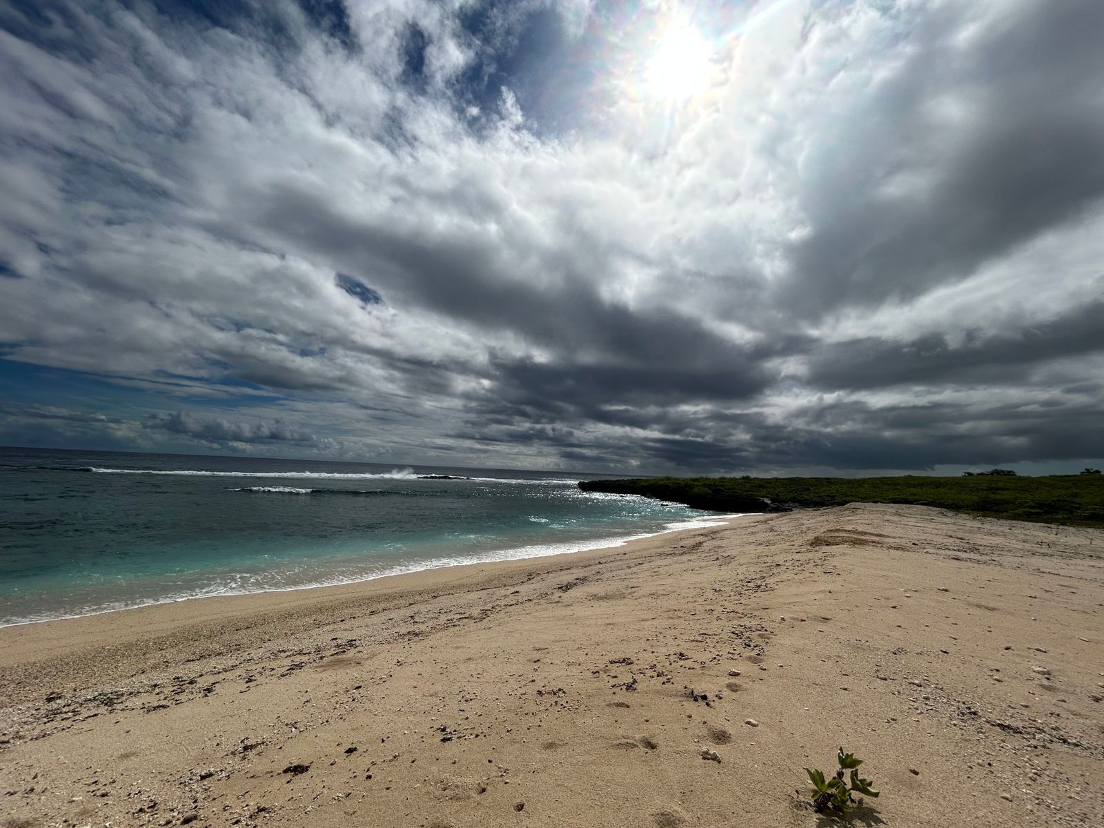 Wolkenverhangener Himmel über einem Sandstrandabschnitt und dem Meer