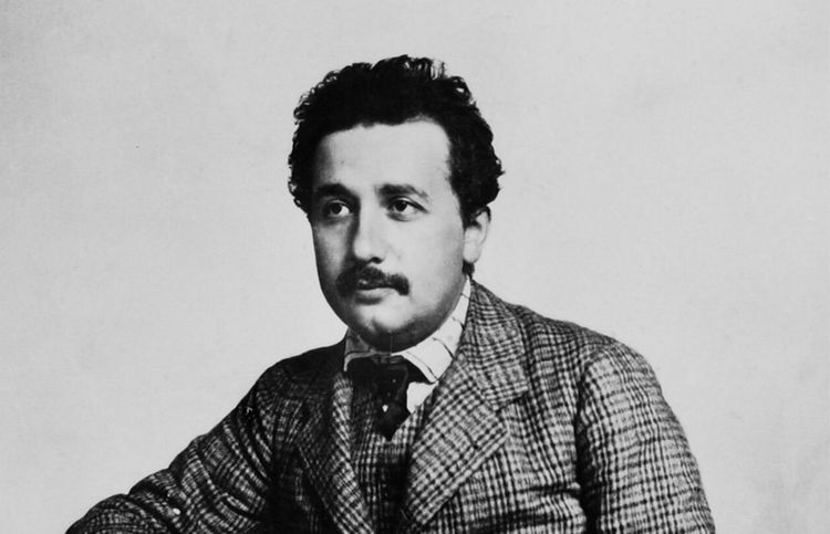 Porträtaufnahme des jungen Albert Einstein in einem dreiteiligen karierten Anzug.