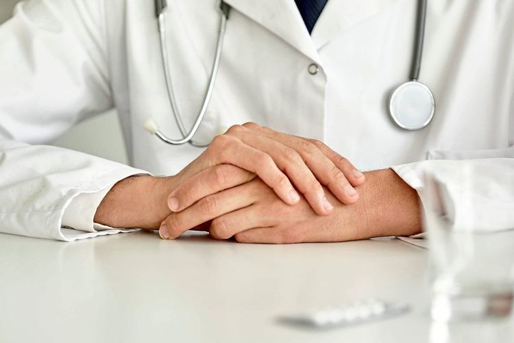 Ein Arzt im weißen Kittel und mit Stethoskop um den Hals sitzt an einem Tisch. 